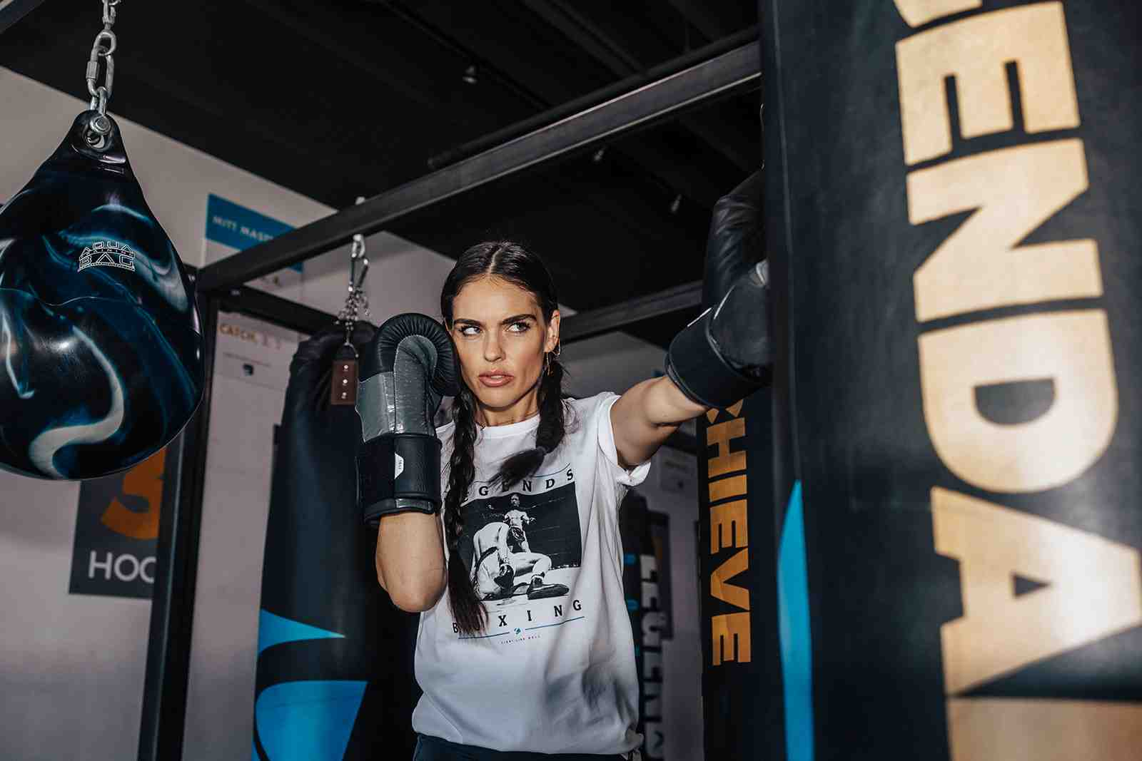 Woman in Legends Boxing white tee and black gloves working the LEGENDARY heavy bag with focus and intensity — boxing for women at Legends Boxing
