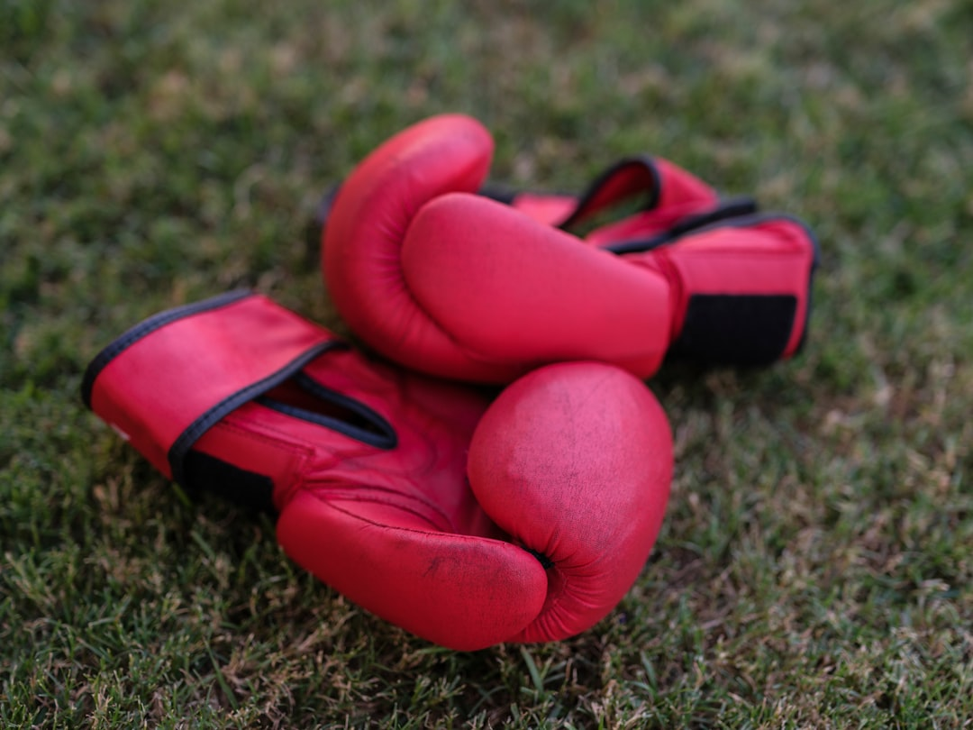 A pair of well-worn red leather boxing gloves resting on green grass — a classic image of the gear you'll need before your first boxing class, and a reminder that the only thing standing between you and Houston's boxing gyms is showing up