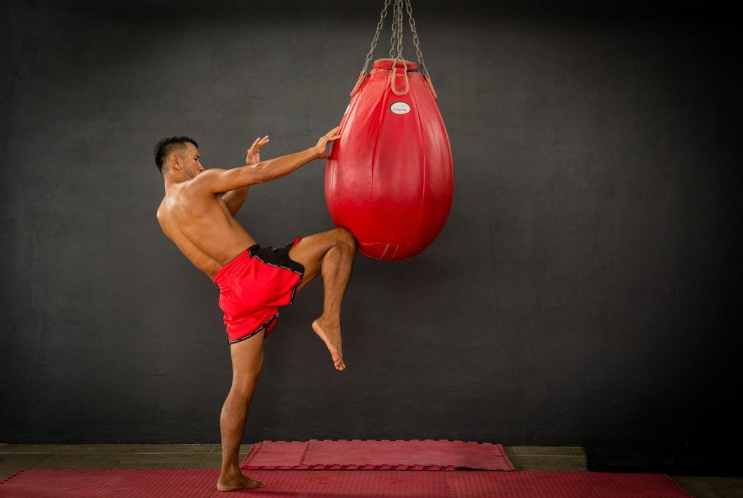 Athlete delivering a powerful roundhouse kick to a large red teardrop heavy bag — kickboxing technique in action at a Salt Lake City boxing gym