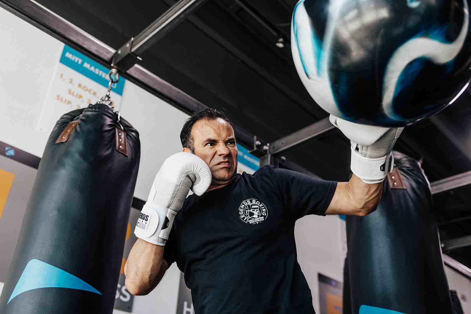 Legends Boxing member in white gloves doing intense close-range bag work with an aggressive uppercut on the speed bag — dramatic low-angle shot showing focus and power