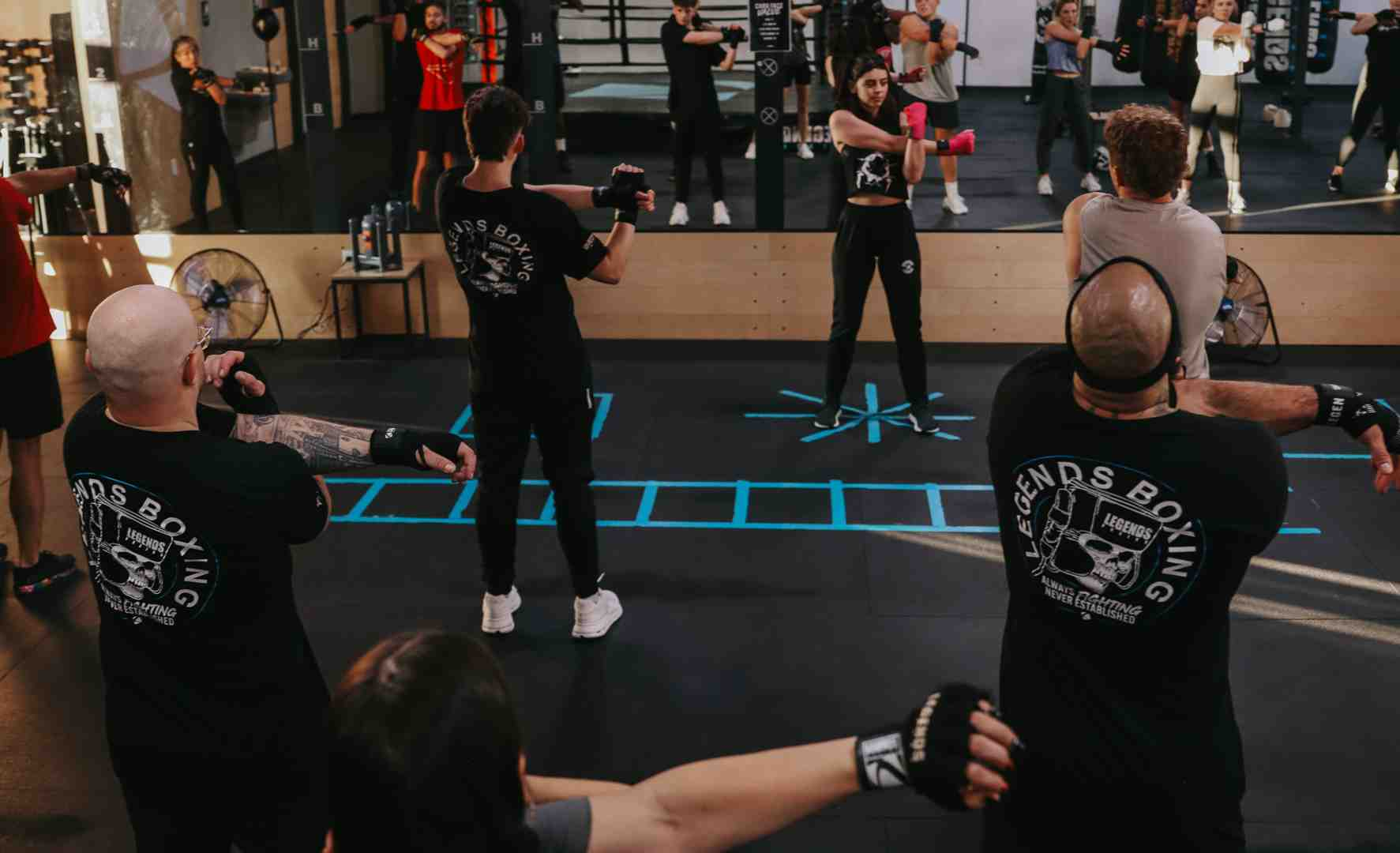 Legends Boxing class with multiple members in black Legends Boxing shirts extending their punches in unison during a shadowboxing drill